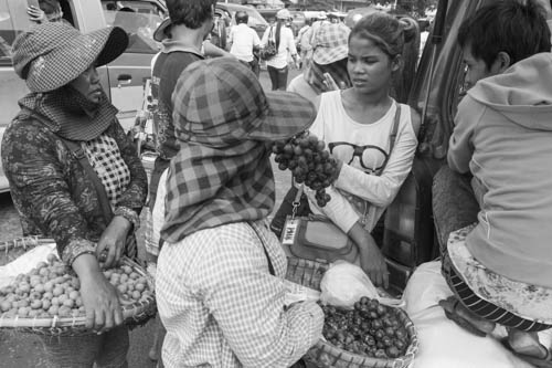 CAMBODIA. Choam Chao (Phnom Penh). 11/10/2012: Young girl buying grapes while waiting for transportation at taxi station before the yearly exodus for 'Pchum Ben' when Cambodians commemorate the deceased.