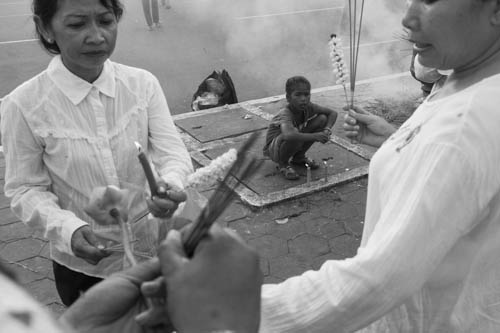 CAMBODIA. Phnom Penh. 31/10/2012: Street child selling fire to worshippers wanting to light their incense sticks in front of the Royal Palace on the 17th day of King Norodom Sihanouk's death. This is also the day he would have celebrated his 90th birthday.