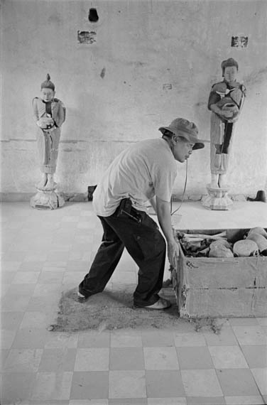 CAMBODIA. Phnom Penh. 1/03/2002: Rithy Panh, film director, moving a crate with skulls during the filming of 'S21' at the Tuol Sleng museum.