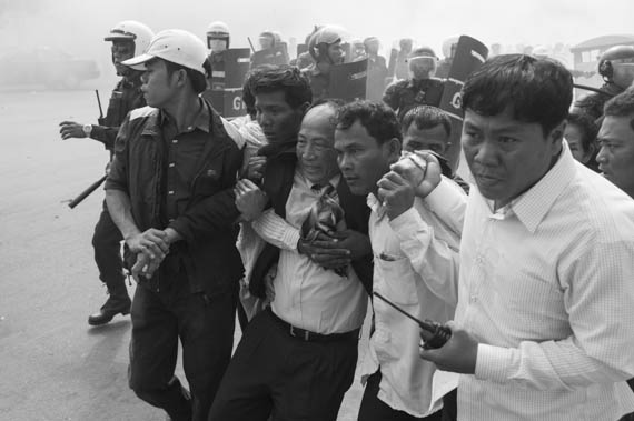 CAMBODIA. Phnom Penh. 27/01/2014: Mam Sonando, Director of Beehive Radio, being whisked away through smoke bombs by supporters during a protest march to the Ministry of Information to request a TV frequency which was dispersed by riot police.