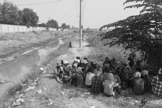 CAMBODIA. Dangkor (Phnom Penh). 28/01/2014: Workers sheltering from the sun while waiting for their representatives to meet with the managers when about 1000 garment factory workers at the industrial area of Vattanac II walked out after 11 union leaders were fired.