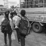 CAMBODIA, Poipet (Banteay Meanchey). 17/06/2014: Asian tourists pass in front of a truck from the Thai immigration returning illegal immigrants to Cambodia. In a massive movement of fear, some 180.000 cambodian migrant workers, many of them illegal, return home in one week time after the military coup in Thailand which vowed to normalise the situation of illegal immigration.