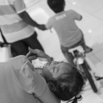 CAMBODIA, Phnom Penh. 1/07/2014: Child sleeping while her brother rides his new nicycle on the first official opening day of the Aeon mall, a 205 million dollar investment by a Japanese microfinance company.